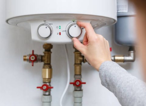 Female hand puts thermostat of electric water heater (boiler) in economy mode. Household enegry saving equipment