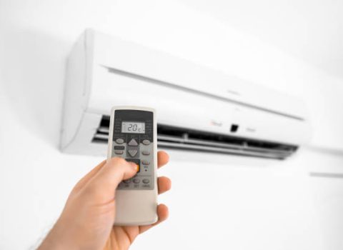 Hand holding remote control in front of the air conditioner.